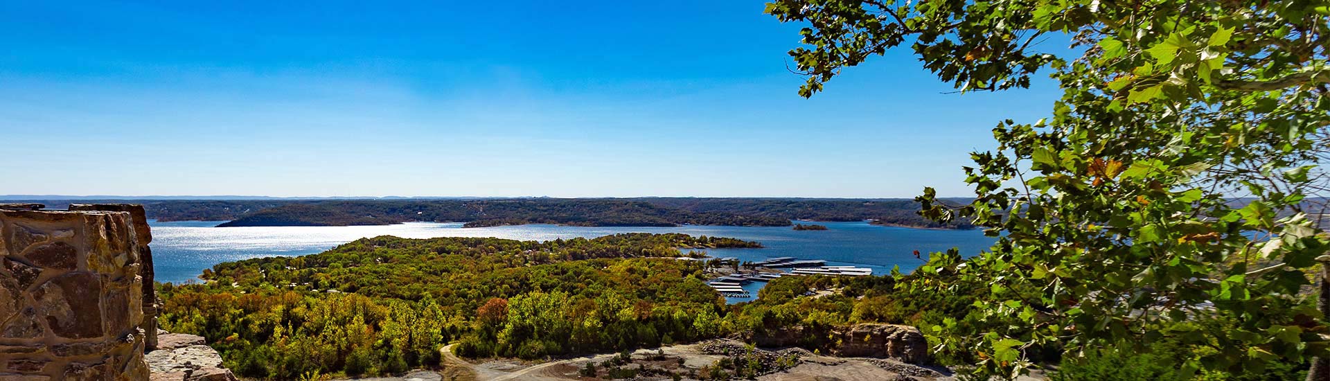 View of Table Rock Lake from atop Baird Mountain with blue sky and framed by trees in foreground, Pink Jeep Tours Branson.