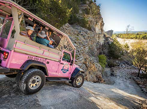 Rear side of a Pink Jeep Wrangler with tour guests inside, descending a winding 4x4 trail into the Baird Mountain Quarry.