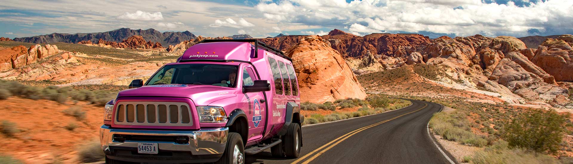 Pink Adventure Tours Las Vegas Tour Trekker driving towards the camera along the Valley of Fire Scenic Byway near Las Vegas, with colorful rock formations in the background.