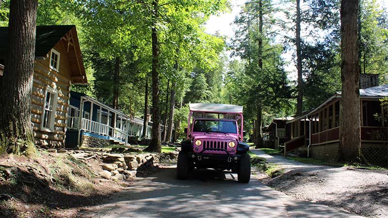 Pink Jeep Wrangler driving past restored cabins at Daisy Town, Elkmont Ghost Town, Great Smoky Mountains National Park.