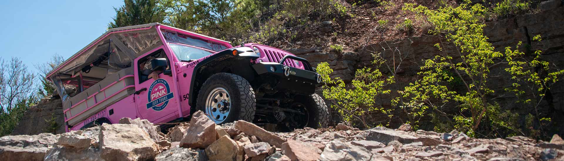 Side view of Pink Jeep Wrangler ascending a steep rocky incline during the Ozark Mountain Crawl Branson Tour..