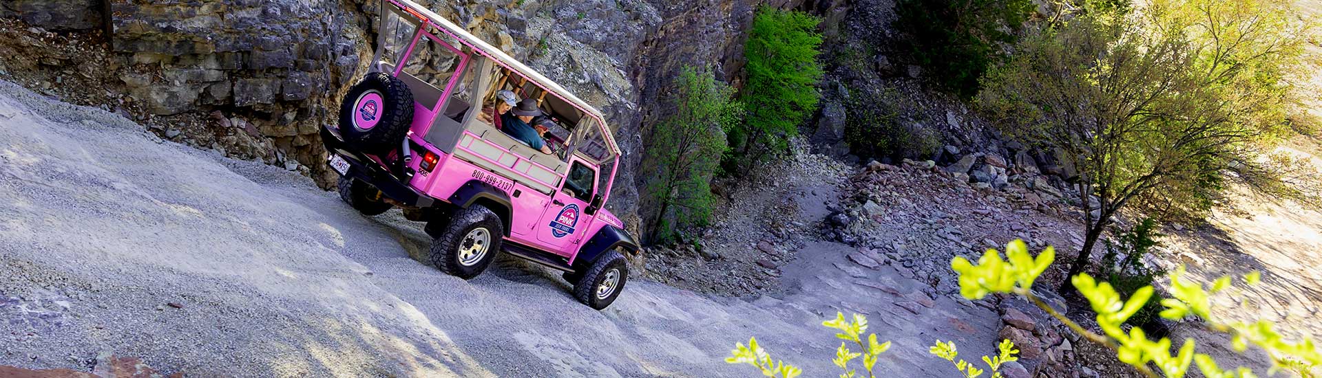 Guests in back of Pink Jeep Wrangler descending steep downhill trail into rock quarry, Ozark Mountains, Branson.