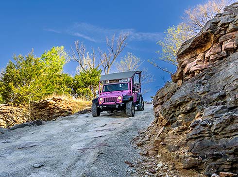 Pink Jeep descending steep, rocky trail alongside Baird Mountain with blue sky, Branson, MO.