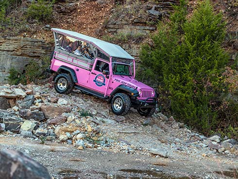 Tour guests riding in Pink Jeep Wangler as it navigates over rocks in quarry below Baird Mountain, Branson.