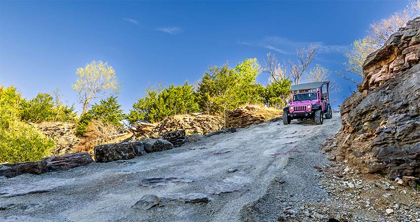 Pink Jeep Wrangler descending from top of steep rocky trail into Baird Mountain Quarry, with blue sky in background.