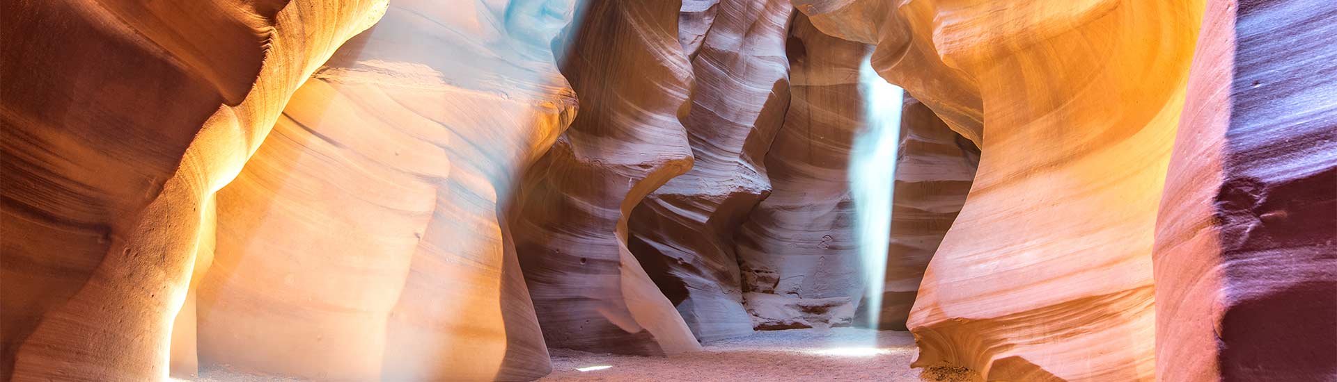 Sunbeams reflect a rainbow of color against the rock formations at the bottom of Lower Antelope Canyon, Page, Arizona, USA