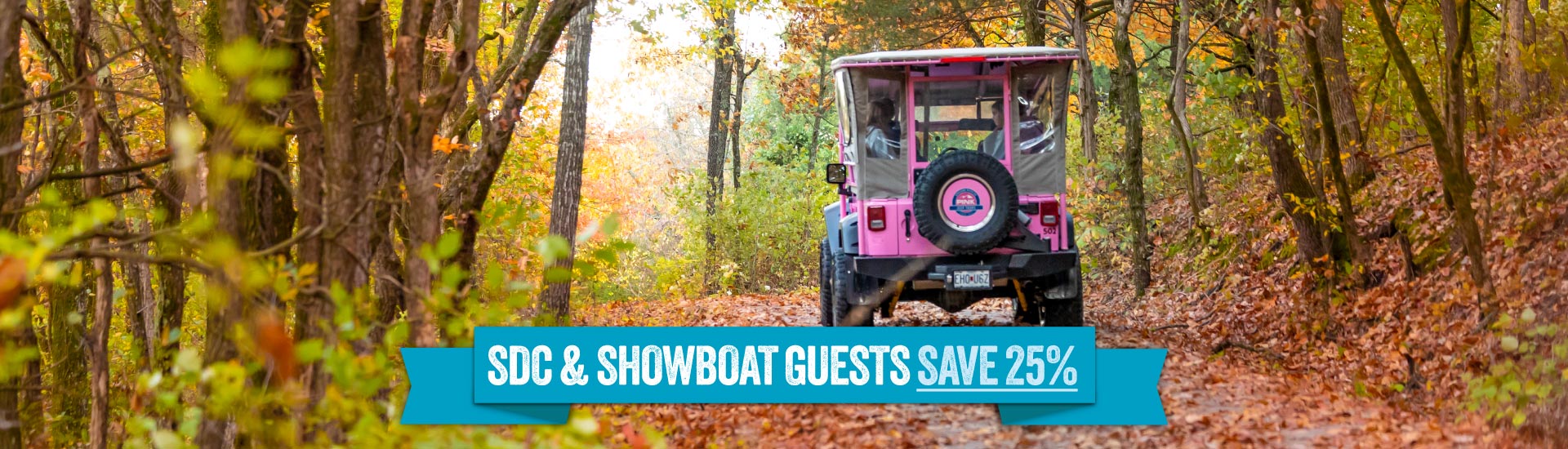 Rear view of a Pink Jeep Tours Jeep Wrangler traveling down an off-road trail flanked by autumn trees in Branson, MO. A banner reads "SDC and Showboat Guests Save 25%."