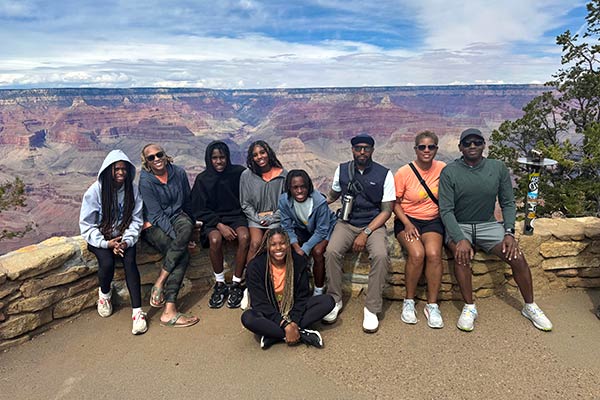 Multigenerational African American family seated on a rock wall with a beautiful view of the Grand Canyon South Rim in the background, Pink Jeep Tours.