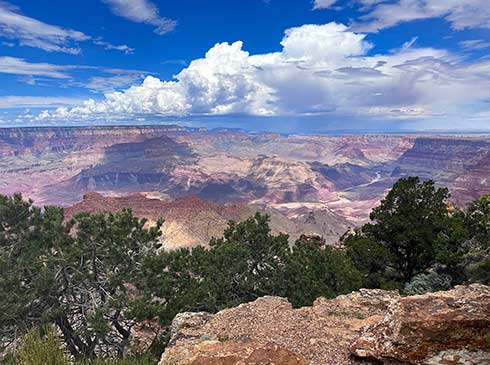 Vast view of the Grand Canyon along Desert View Drive with scattered clouds, showcasing layered rock formations and a winding river below.
