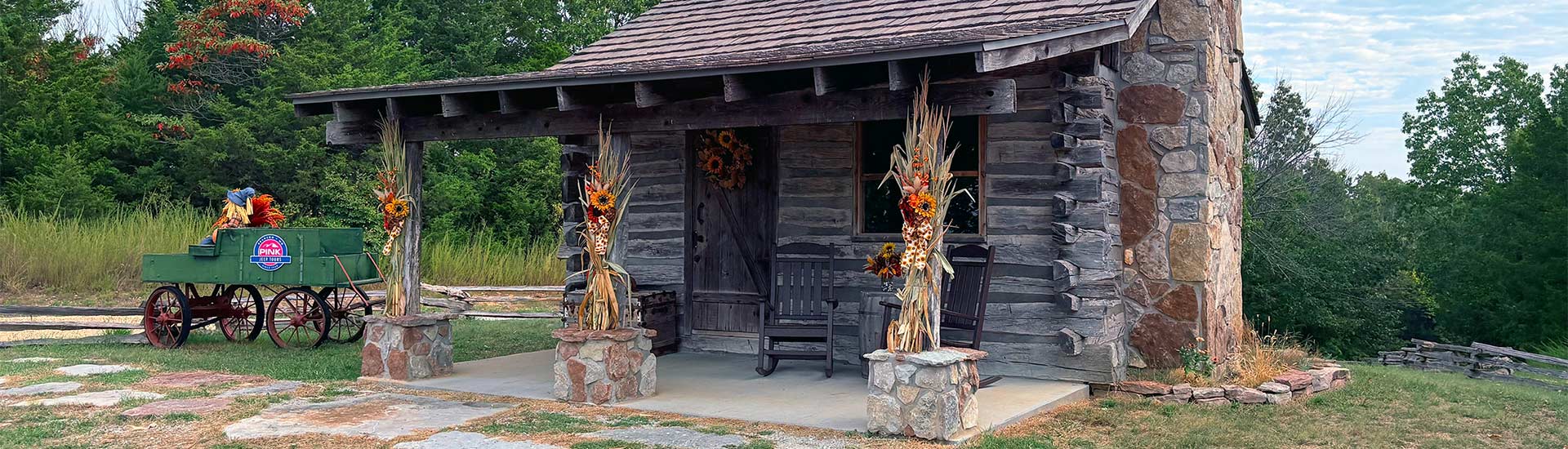 Historic Baird Mountain Cabin decorated for fall season, with autumn trees blooming in the background, Pink Jeep Tours Branson.