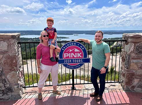 Parents and cute redheaded boy on mom's shoulder posing on the Baird Mountain patio overlooking Table Rock Lake in summer, Branson, MO.