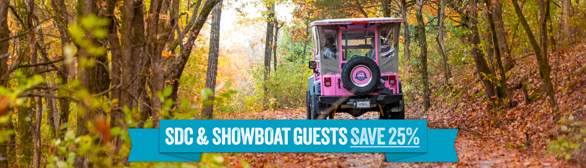 Rear view of a Pink Jeep Tours Jeep Wrangler traveling down an off-road trail flanked by autumn trees in Branson, MO. A banner reads "SDC and Showboat Guests Save 25%."