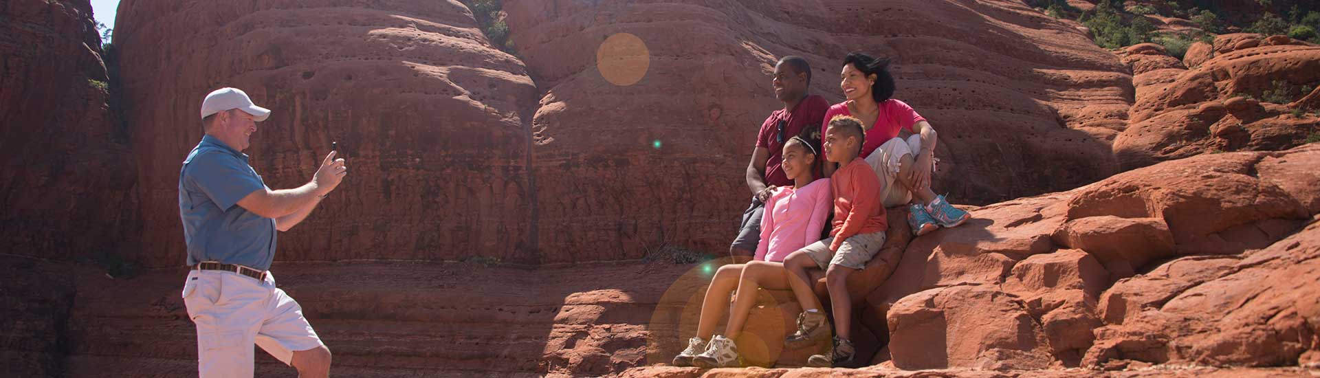 Pink Jeep Tours Sedona tour guide taking a photo of a family seated on red rock formations, Broken Arrow Trail, Sedona, AZ.