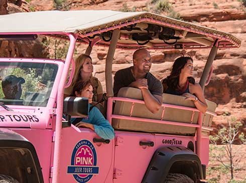 Close-up image of guide and three guests seated in a Pink® Jeep® looking out at Sedona's red rocks