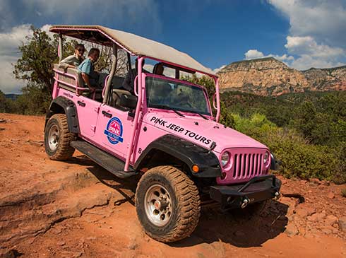 A customized Pink® Jeep® with guests navigates down a rugged rock slope on the Coyote Canyons tour