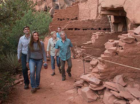 Four guests on Pink Jeep's Ancient Ruins tour walk past 700-year-old cliff dwellings at the Honanki Heritage Site near Sedona