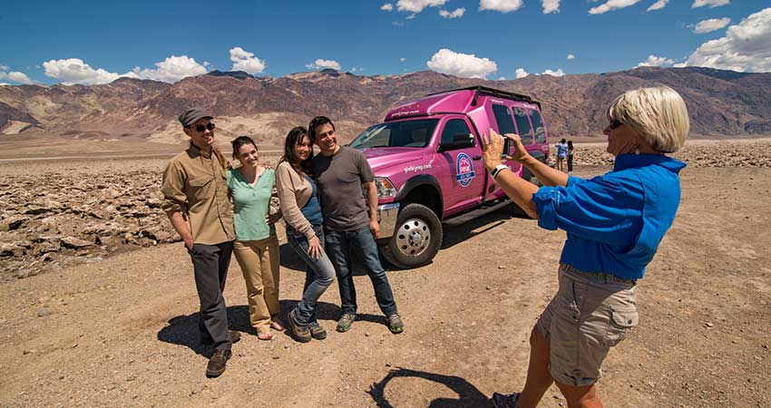 Tour guide taking photo of Pink Jeep Death Valley Tour guests with Devil’s Golf Course and Pink Tour Trekker in background.
