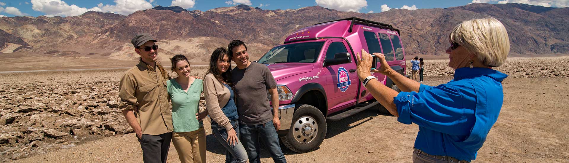 Tour guide taking guests' photo next to Pink Adventure Tour Trekker at the Devil’s Golf Course, Death Valley National Park.