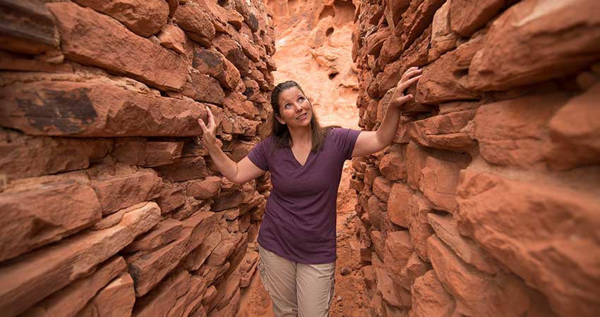 Woman walking through the narrow passages between the 1930s sandstone Cabins at Valley of Fire State Park.