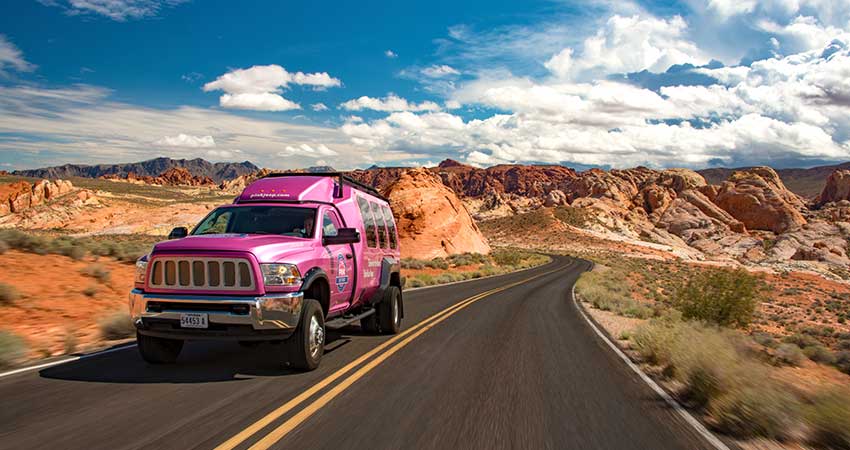 Pink Jeep Tour Trekker driving along a blacktop road winding through the colorful landscape of Valley of Fire State Park.