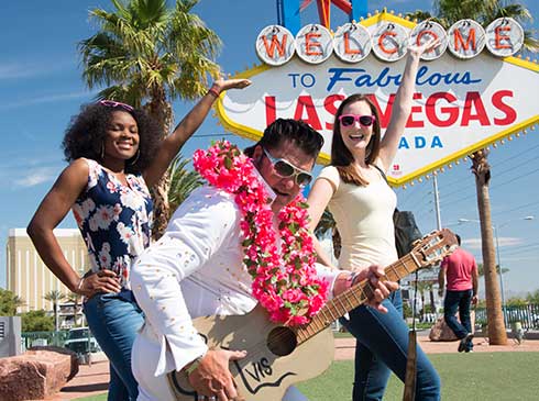 Two Pink Jeep tour guests pose with Elvis in front of famous "Welcome to Fabulous Las Vegas" sign
