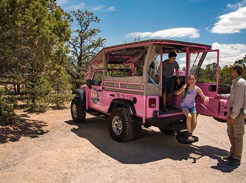 Two kids exiting the rear of a Pink® Jeep® Wrangler during the Trail of Time Tour with guide nearby