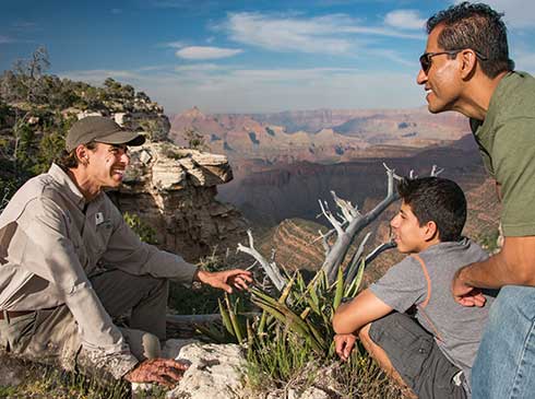 Pink® Jeep® guide explaining southwest desert vegetation to father and son with Canyon view in background
