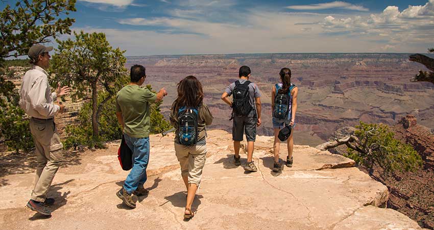Grand Entrance Sunset guests walk out towards a viewpoint at the canyon's South Rim, with the rugged canyon walls in the distance.