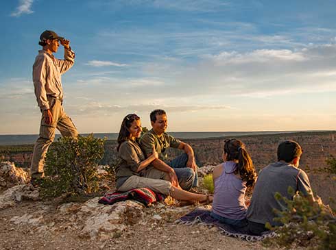 Grand Entrance Sunset guests sit at Canyon's edge during twilight with Pink Jeep guide looking off into sunset