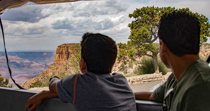 Father and sun looking out from the back of a Pink Jeep® Wrangler towards a beautiful view of the Grand Canyon.
