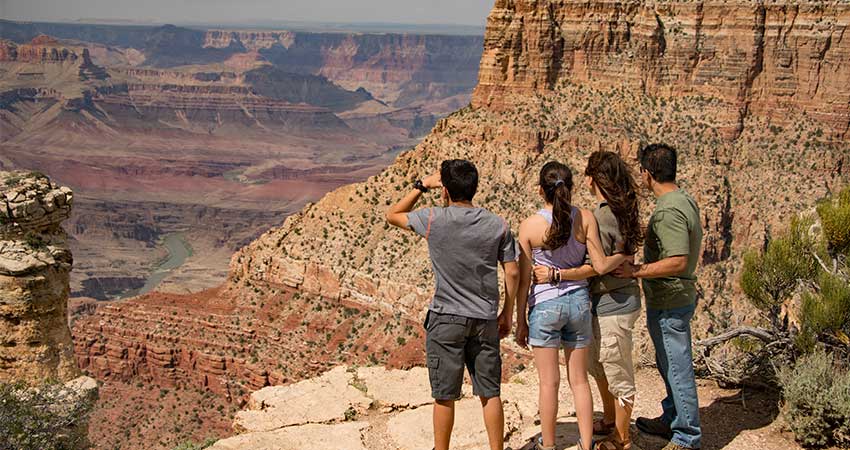 Family standing at the edge of the Grand Canyon's South Rim enjoying a view along the Desert View Sunset tour.