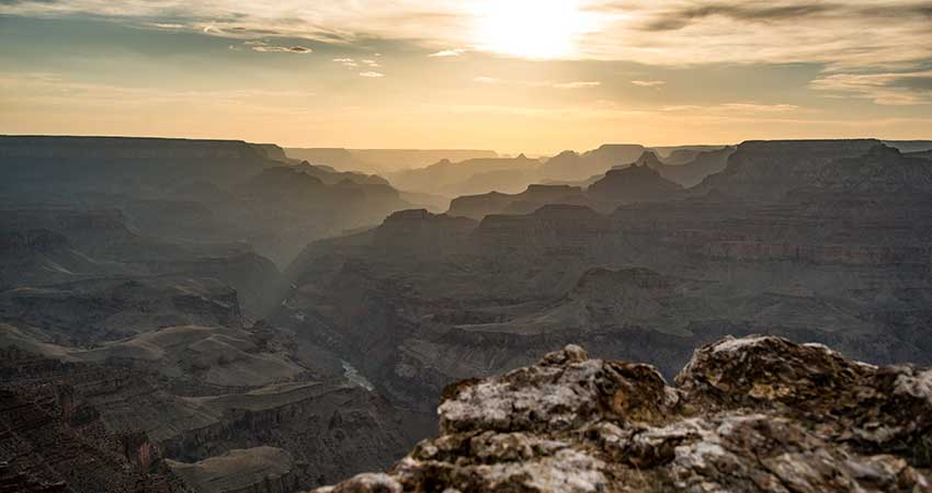 A stunning golden Grand Canyon Sunset with the jagged, shaded canyon rims in the foreground.