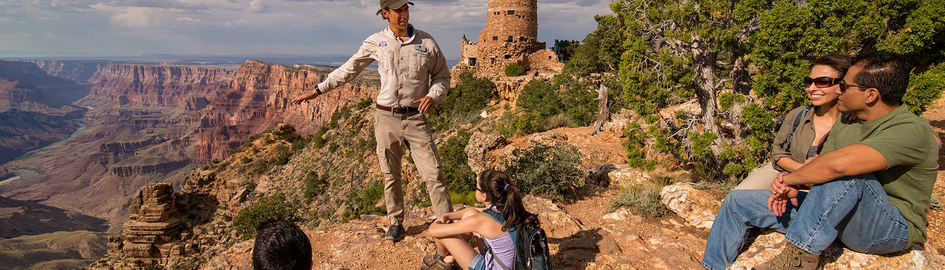 Pink Adventure tour guide with family seated on the Grand Canyon's South Rim with Desert View Watchtower in the distance.