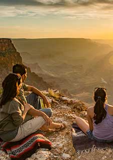 Vertical image of a family seated on the edge of the Grand Canyon's South Rim watching a golden sunset on the Desert View tour.