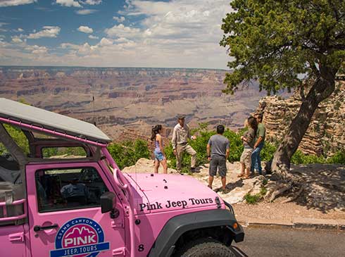 Tour guests overlooking panoramic view of Grand Canyon South Rim with Pink® Jeep® in foreground.