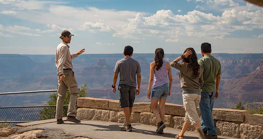 Pink Jeep Tour guide points out the geological layers of the Grand Canyon at a viewpoint with a family of guests..
