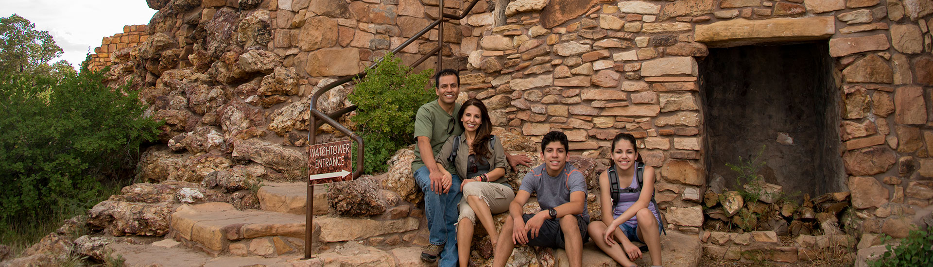 Family of four seated next to the stairs outside the Grand Canyon Desert View Watchtower.
