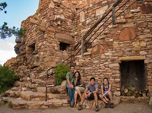 Family of four seated by the exterior stairway of Grand Canyon Desert View Watchtower.