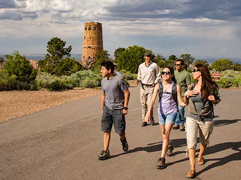 Pink Jeep Tour guide leading a family on a walk, passing the Grand Canyon South Rim watchtower.