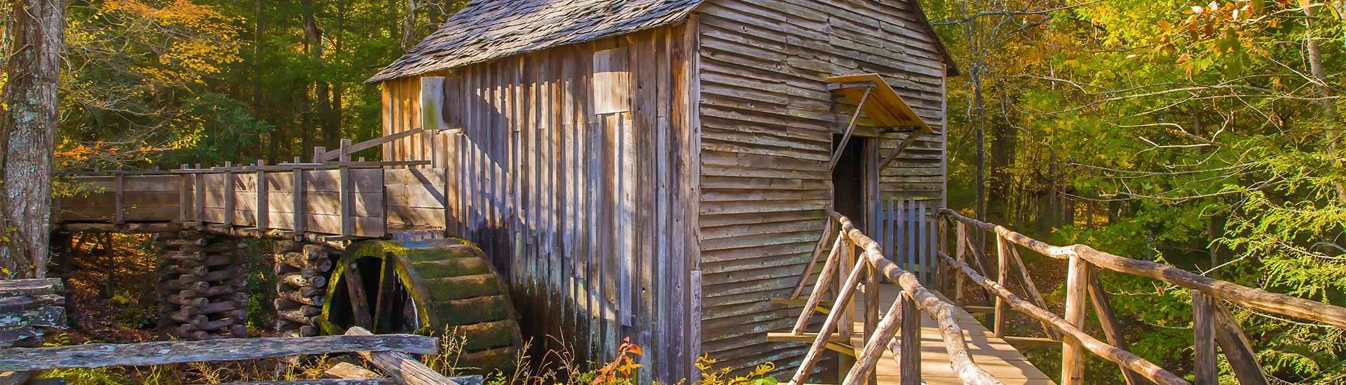 Closeup of the John P. Cable Grist Mill and water wheel among fall trees in the Cades Cove region of the Great Smoky Mountains.