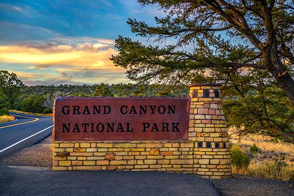 Grand Canyon National Park South Entrance sign at dusk with a beautiful sun setting in the background.