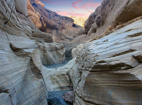 Sunrise over Mosaic Canyon lights the narrow canyon trail flanked by smooth, colorful mosaic breccia at Death Valley National Park.