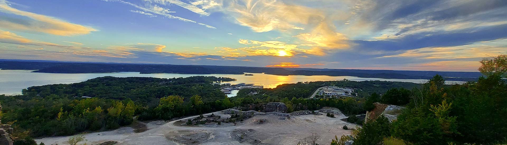View of Branson's Table Rock Lake and the quarry below Baird Mountain at twilight, with a yellow sun dipping behind violet blue clouds.