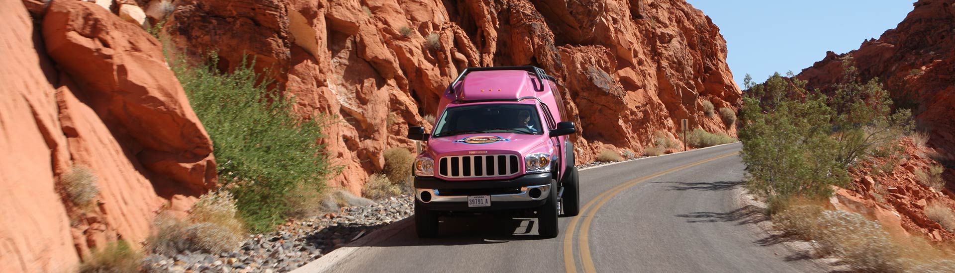Pink Jeep Tours Adventure Tour Trekker driving towards camera flanked by towering red rocks in Red Rock Canyon National Conservation Area.