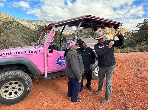 Pink Jeep Tours adventure guide taking a selfie with two tour guests at Red Rock Canyon with a Pink Jeep Wrangler in the background.
