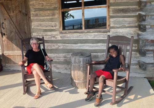 A lady and young boy relax in rockers on a log cabin front porch atop Baird Mountain in Branson, MO