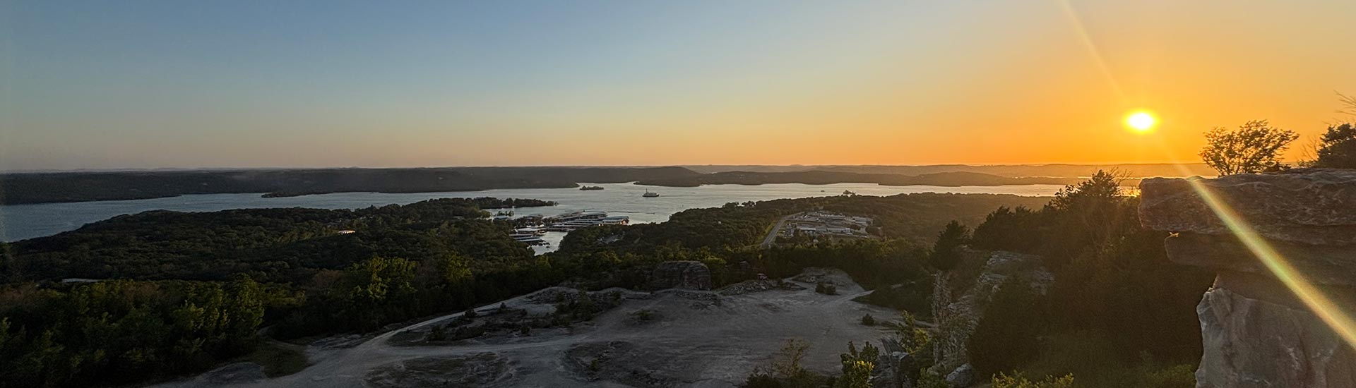 A golden sun orb casts a flare over Pink Jeep Tours' Rock Quarry off-road course at dusk, with Table Rock Lake in the distance.