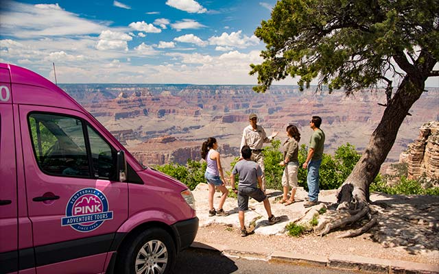 Pink Jeep Tour guide and guests standing at the edge of the Grand Canyon's South Rim with a Pink Adventure Tour Trekker parked in the foreground.