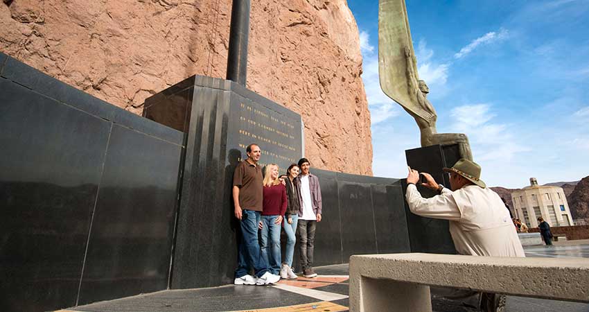 Las Vegas Pink Jeep tour guide taking a photo of two couples standing near the Winged Figures of the Republic statue at Hoover Dam.