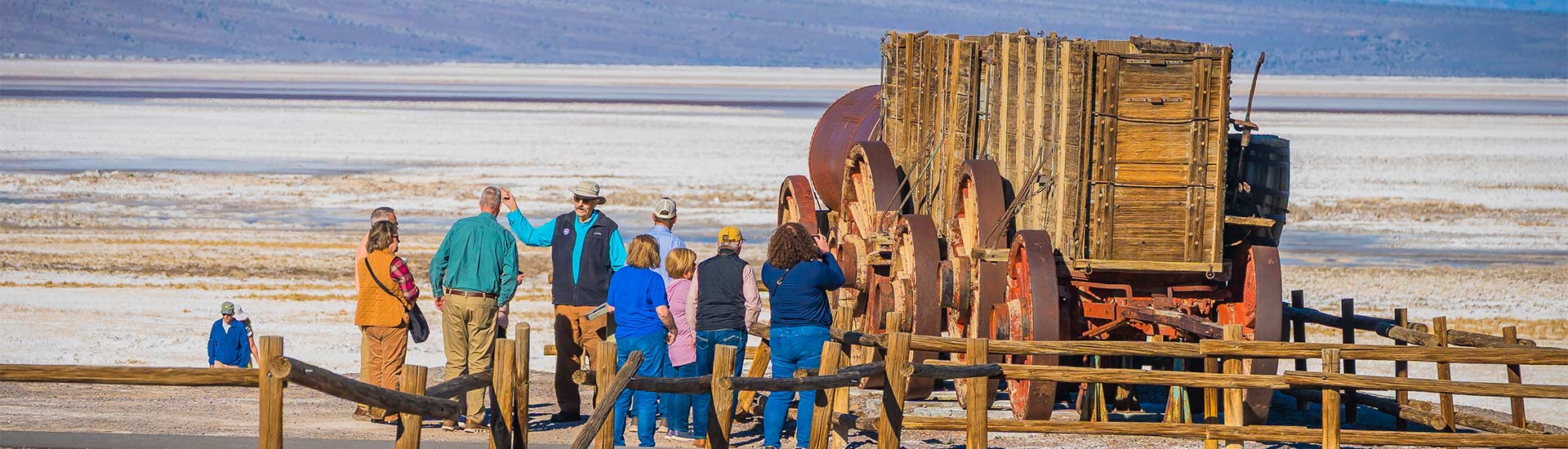 Pink Jeep Tours Las Vegas guide talking to a group of tour guests next to the Twenty Mule Team Replica at Death Valley National Park. 